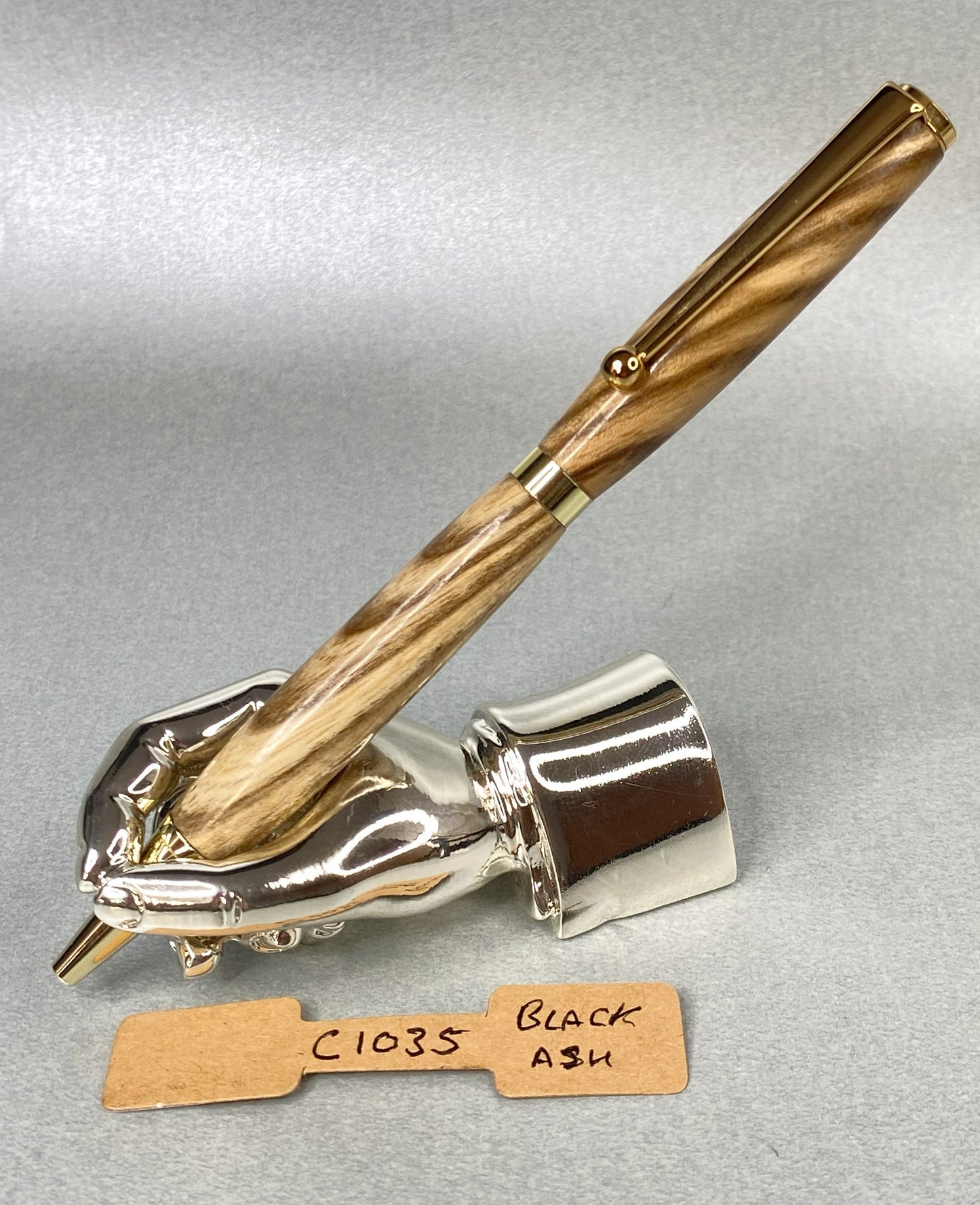 Black ash wood pen with gold plated fittings on a chrome plated stand in the shape of a hand