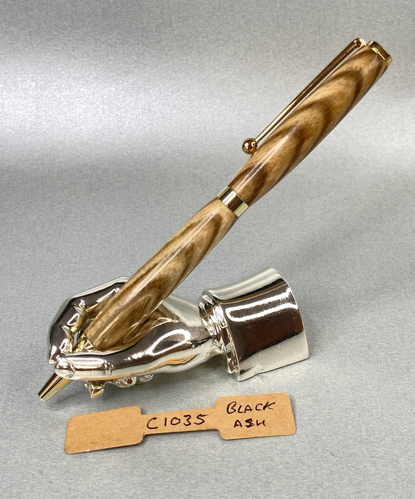 Black ash wood pen with gold plated fittings on a chrome plated stand in the shape of a hand