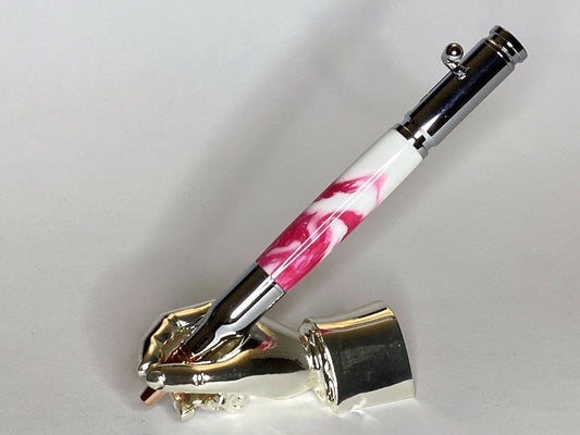 A right hand shaped metal base holding a handturned pink & white Polyester acrylic Bolt action pen as you would hold it to write with.