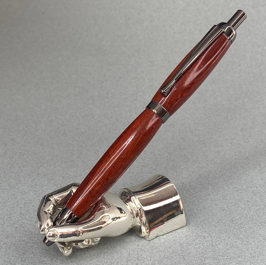 A right hand shaped metal base shown holding a handturned Paduk wood pen as you would hold it to write with.